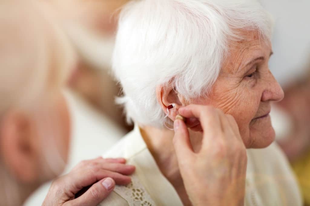 Female doctor applying hearing aid to senior woman's ear