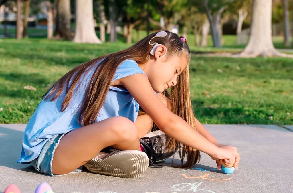 Girl with cochlear implant playing with sidewalk chalk